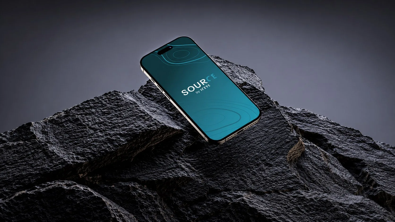 Telefon z ekranem startowym aplikacji SOURCE by ICEYE leżący na ciemnej skale